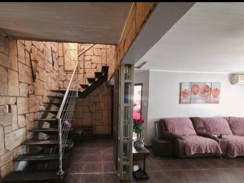 Open plan living area featuring a striking stone feature wall, a modern metal staircase with stainless steel balustrades, and tiled flooring throughout.