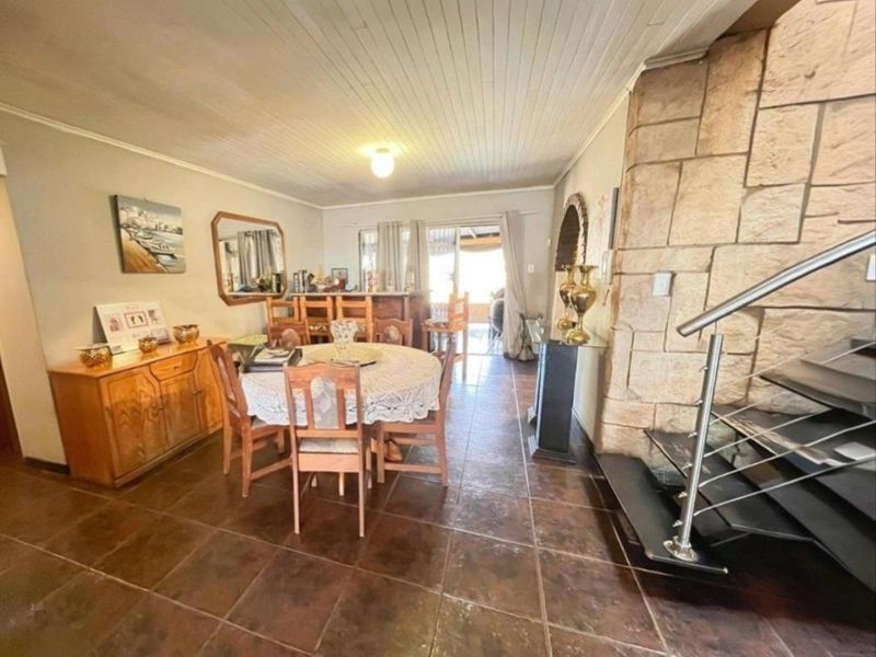 Open plan living and dining area featuring a stone feature wall, tiled flooring, and a staircase with a modern metal railing.