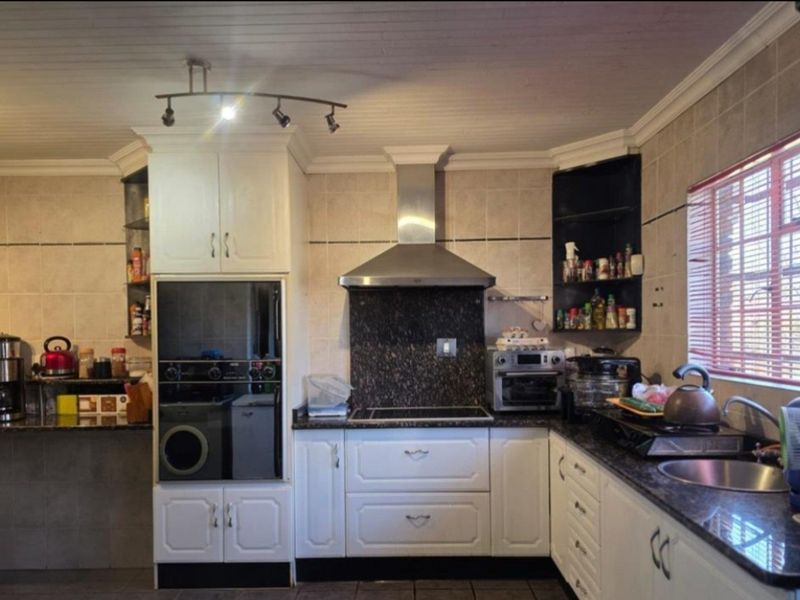 Functional kitchen featuring white cabinetry, granite countertops, a built-in oven, and a stainless steel extractor fan with tiled backsplash.