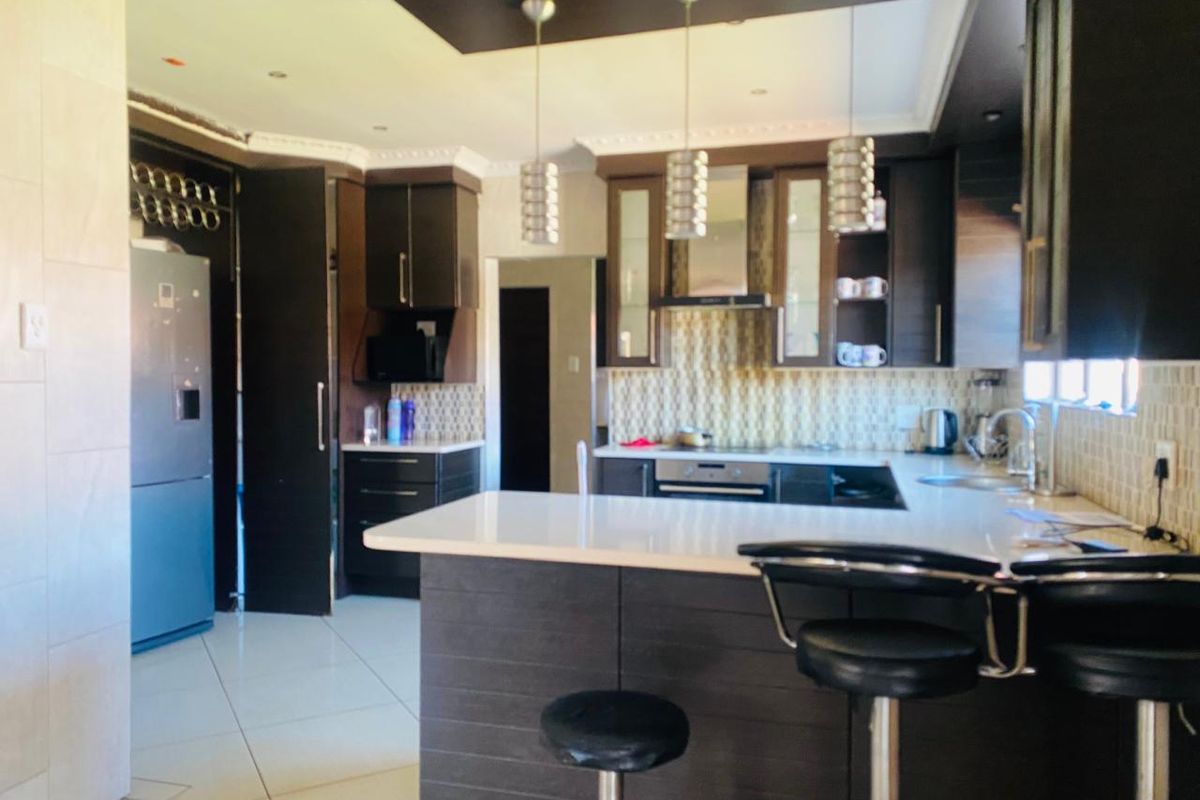 Modern kitchen featuring dark wood cabinetry, stone countertops, integrated appliances, and a breakfast bar with pendant lighting.