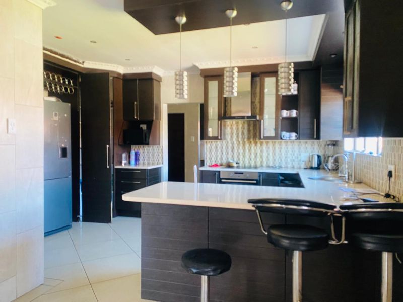 Modern kitchen featuring dark wood cabinetry, stone countertops, integrated appliances, and a breakfast bar with pendant lighting.
