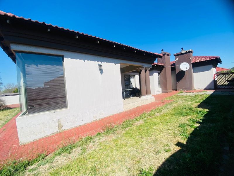 Rear view of the property featuring a covered patio, tiled roof, and a brick-paved walkway leading along the exterior wall.