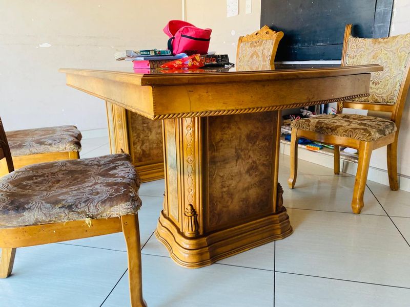 A dining area featuring tiled flooring and plain walls, currently furnished with a traditional wooden dining set.