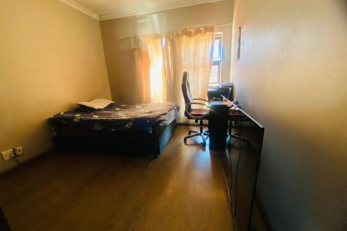 A standard bedroom featuring laminate flooring and decorative cornice detailing, providing a functional space with natural light from the window.