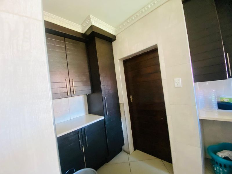 A clean and functional scullery area featuring dark wood built-in cabinetry, stone countertops, and elegant crown molding details.