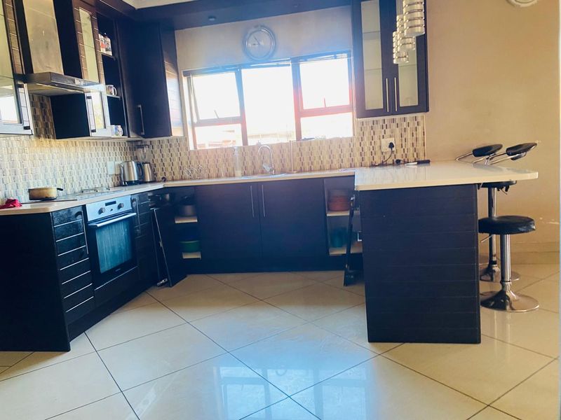 Modern kitchen featuring dark wood cabinetry, stone countertops, a central island, mosaic tile backsplash, and built-in appliances with polished ceramic floor tiles.