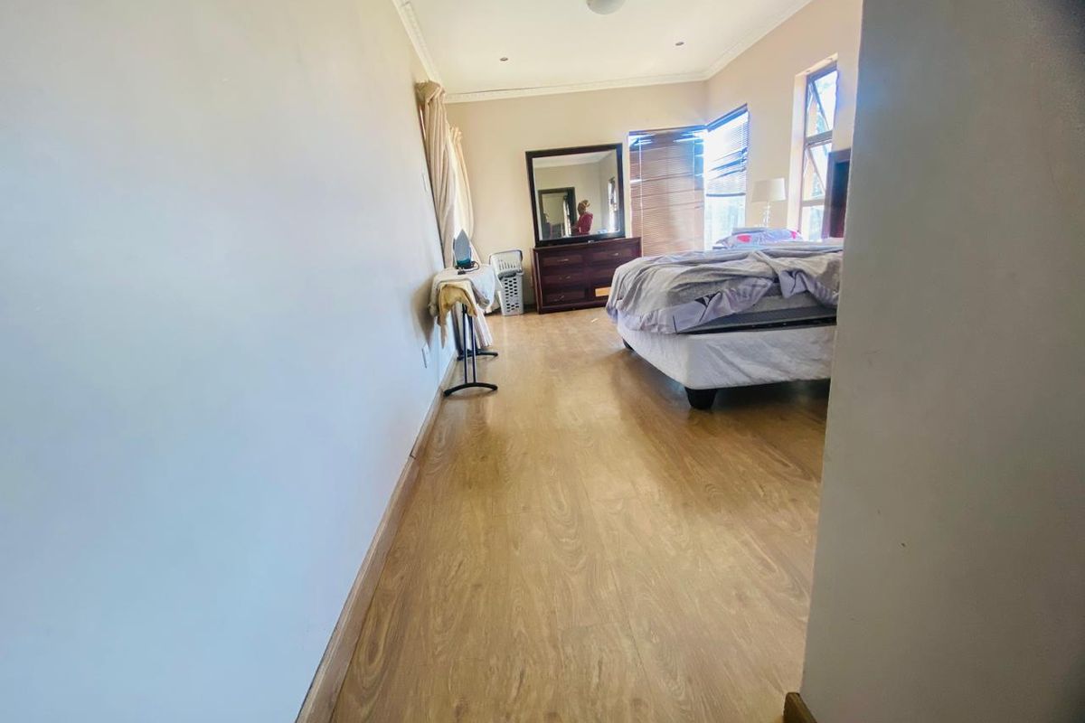 A spacious bedroom featuring light-toned laminate flooring, neutral wall finishes, and large windows with fitted blinds.