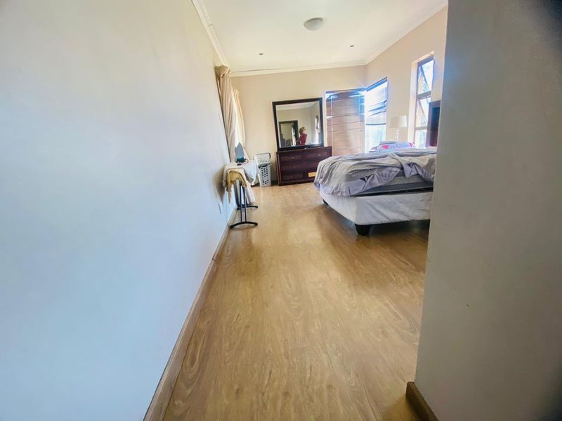 A spacious bedroom featuring light-toned laminate flooring, neutral wall finishes, and large windows with fitted blinds.