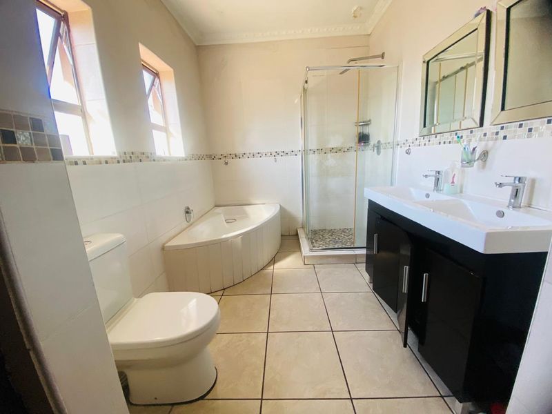 A functional bathroom featuring a corner bathtub, a separate glass-enclosed shower, and a modern double vanity with storage cabinetry.