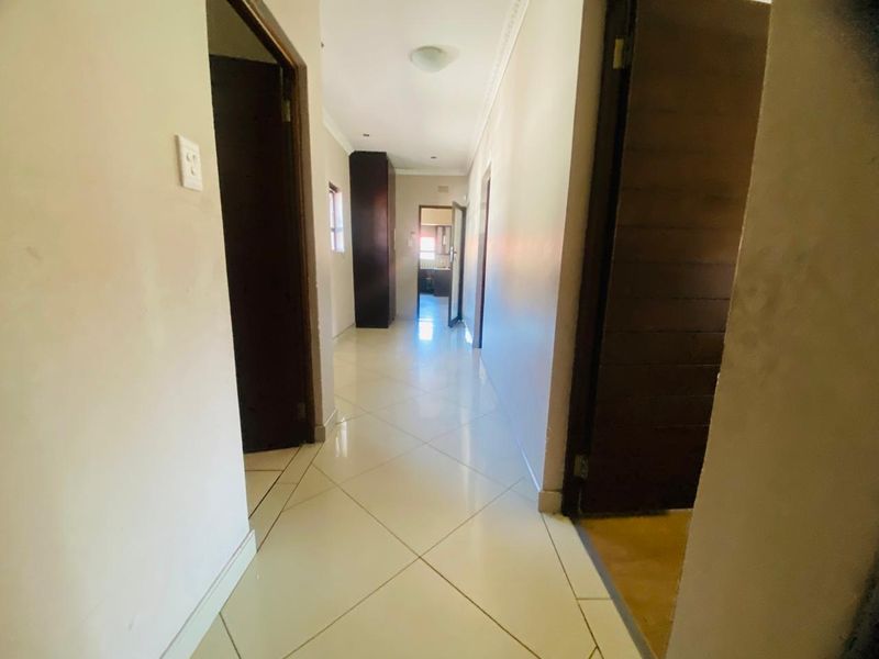 A bright, tiled hallway featuring neutral walls, coving, and built-in storage, providing access to multiple rooms within the home.
