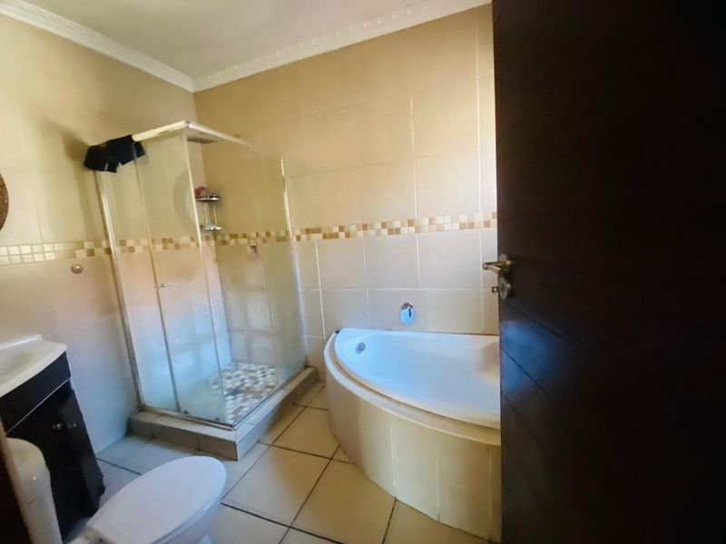 A functional bathroom featuring a corner bathtub, a separate glass-enclosed shower, and tiled finishes throughout.