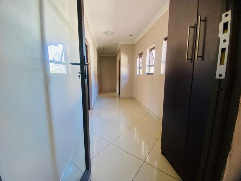 A bright, tiled hallway featuring built-in storage cupboards and decorative ceiling cornicing, providing a clean and functional transition space within the home.