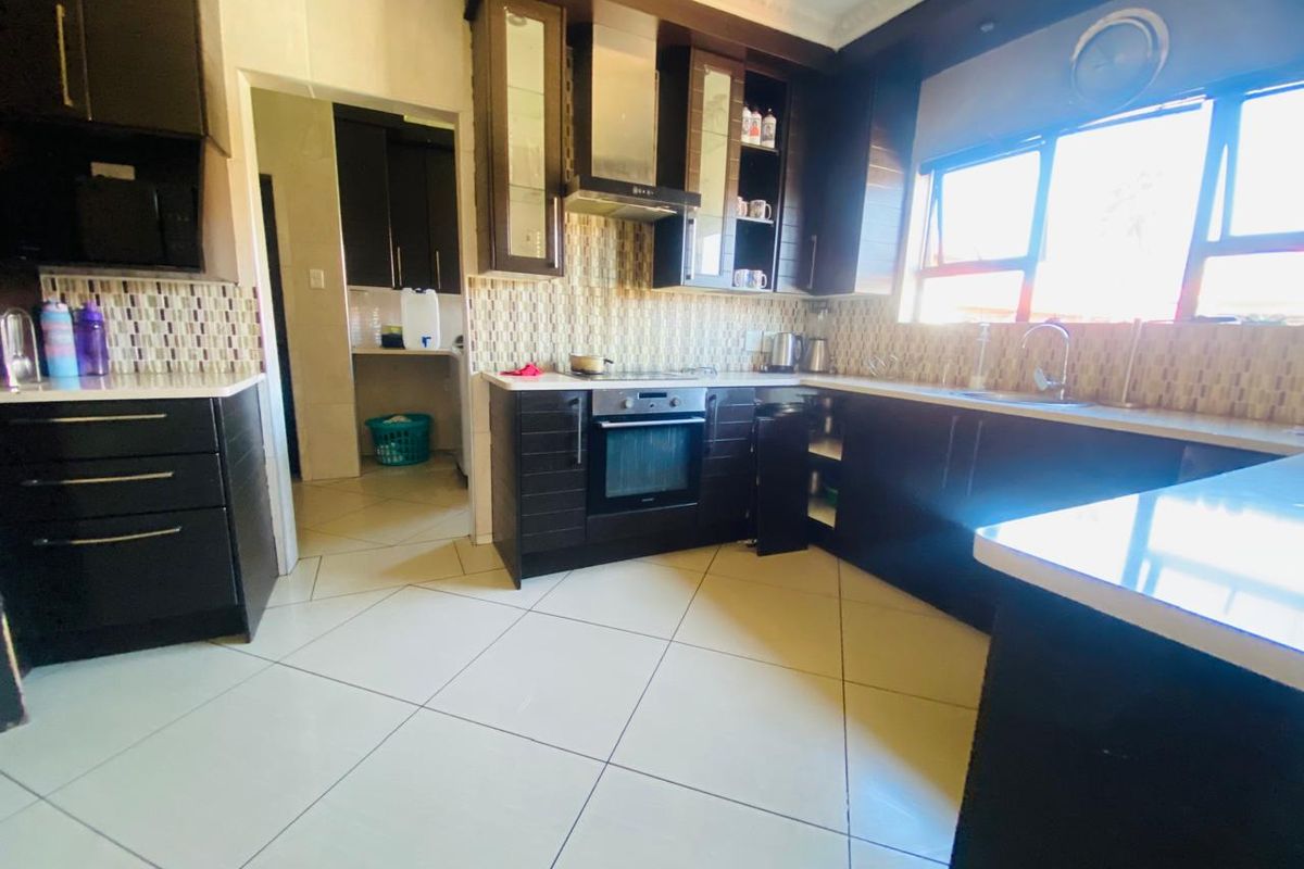 A functional kitchen featuring dark cabinetry, stone countertops, mosaic tile backsplash, and built-in appliances, with an adjacent scullery area.