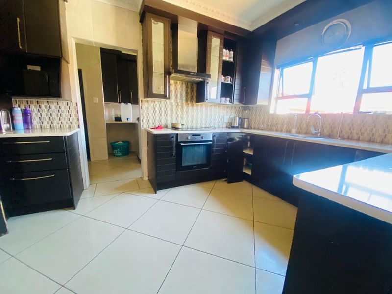 A functional kitchen featuring dark cabinetry, stone countertops, mosaic tile backsplash, and built-in appliances, with an adjacent scullery area.