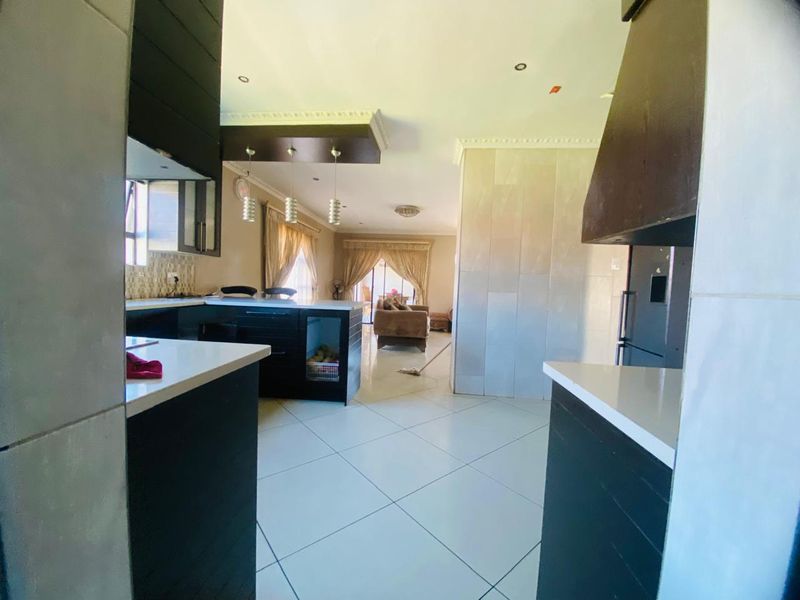 Open-plan kitchen and living area featuring modern dark cabinetry, stone countertops, tiled flooring, and recessed lighting, creating a cohesive and functional living space.
