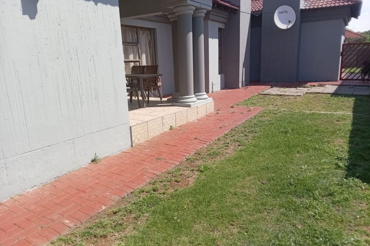 Rear view of the property featuring a covered patio with concrete columns, brick paved walkway, and a small garden area.