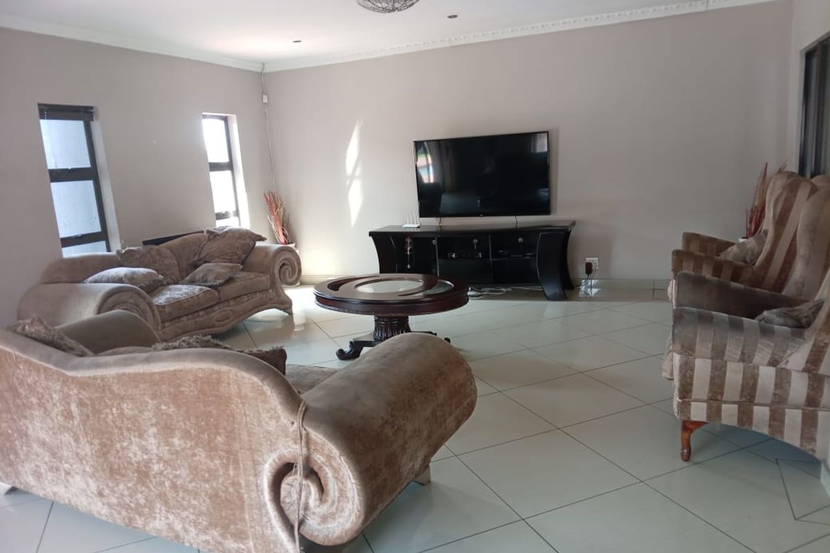 Spacious living room featuring neutral wall tones, large format floor tiles, and decorative ceiling cornicing, providing a comfortable and well-lit family area.