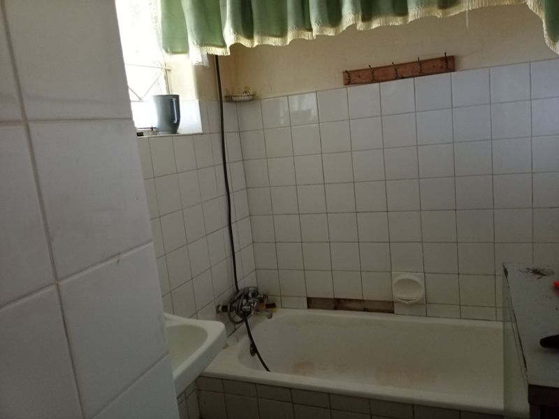 A dated bathroom featuring a bathtub and basin with white wall tiling, currently requiring maintenance and cosmetic updates to the wall finishes.