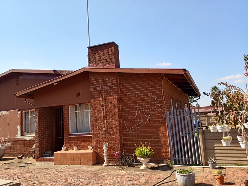 Rear view of a single-story brick house featuring a prominent chimney, tiled entrance step, and metal security gate.