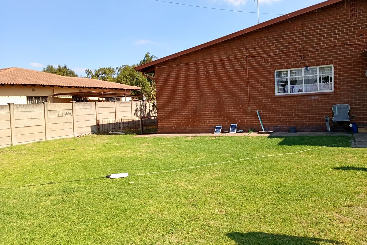 A view of the rear garden featuring a red brick exterior wall, a precast concrete boundary fence, and a well-maintained lawn area.