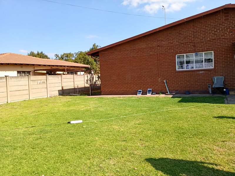 A view of the rear garden featuring a red brick exterior wall, a precast concrete boundary fence, and a well-maintained lawn area.