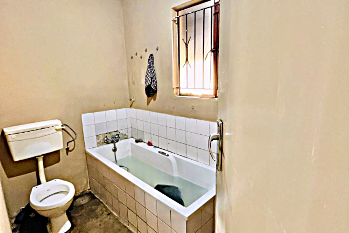 A basic bathroom featuring a bathtub, toilet, and tiled splashback, requiring significant renovation and cosmetic updates to improve its condition and functionality.