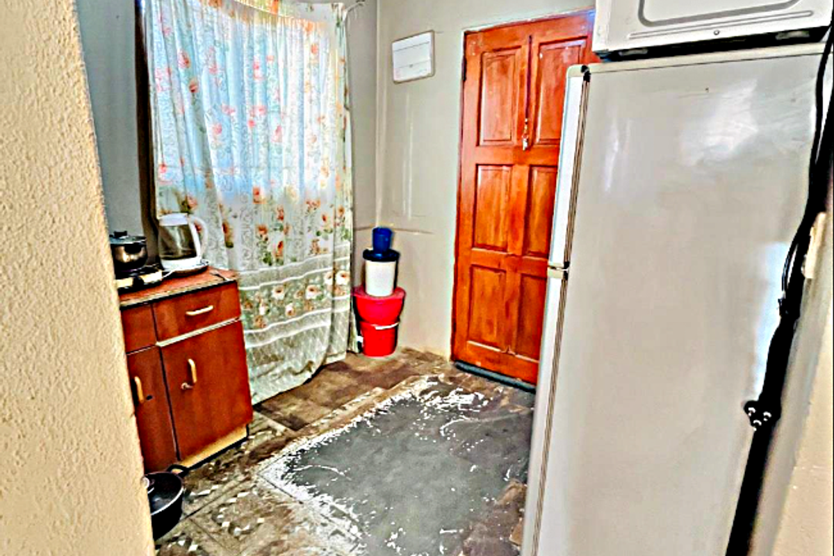 A small kitchen area featuring built-in cabinetry and a wooden door, currently showing significant wear to the flooring and wall finishes.