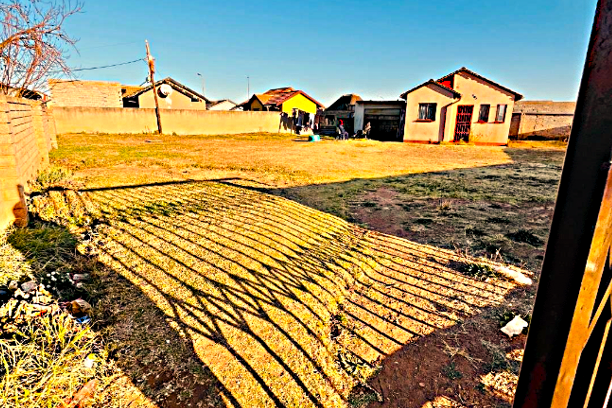 A view of the rear yard area featuring a perimeter wall and metal gate access, with an expansive unpaved ground surface.