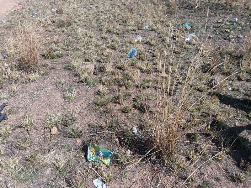 A view of the vacant residential land showing dry grass and scattered litter across the plot.