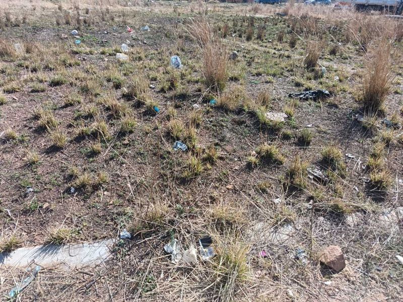 A vacant residential plot featuring dry, unmaintained grass and scattered debris, suitable for future development.