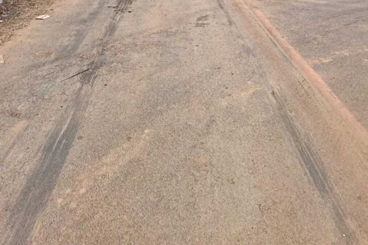 A view of the asphalt street providing access to the vacant residential land, showing signs of wear and surrounding debris.