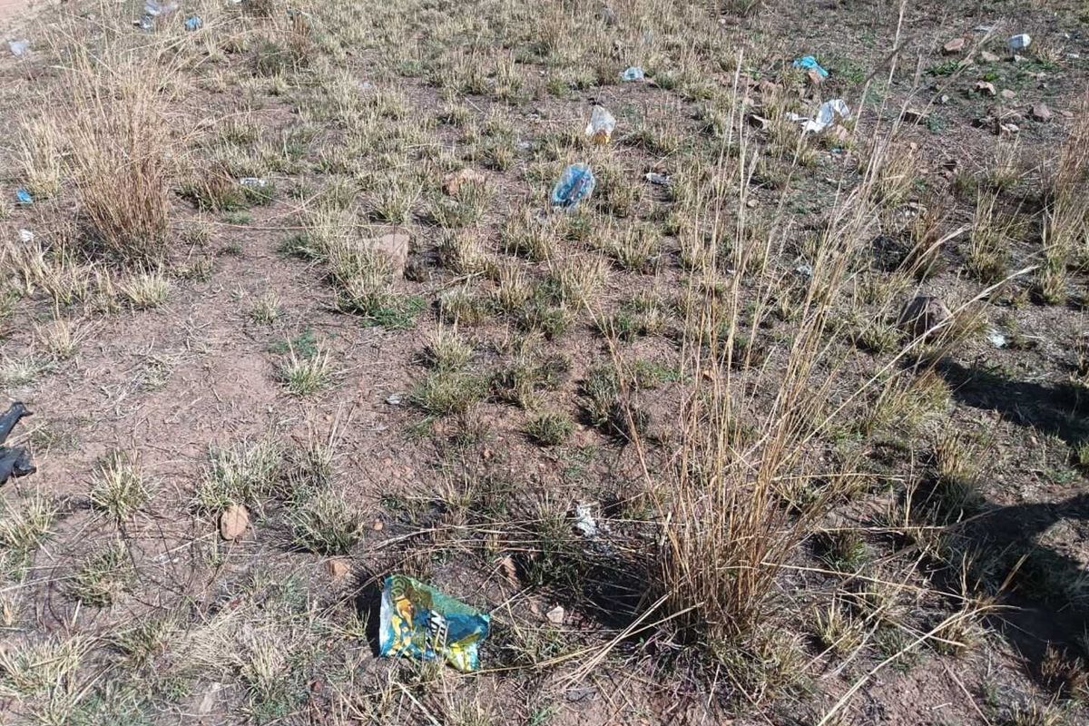A view of the vacant residential land showing dry grass and scattered litter across the plot.