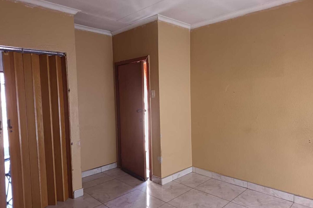 An empty living area featuring tiled flooring, a folding door, and neutral wall finishes, offering a blank canvas for potential interior design updates.