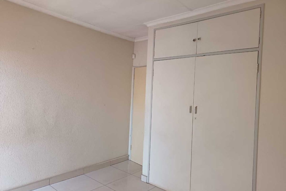 An empty bedroom featuring neutral wall tones, tiled flooring, and built-in cupboards with overhead storage compartments.