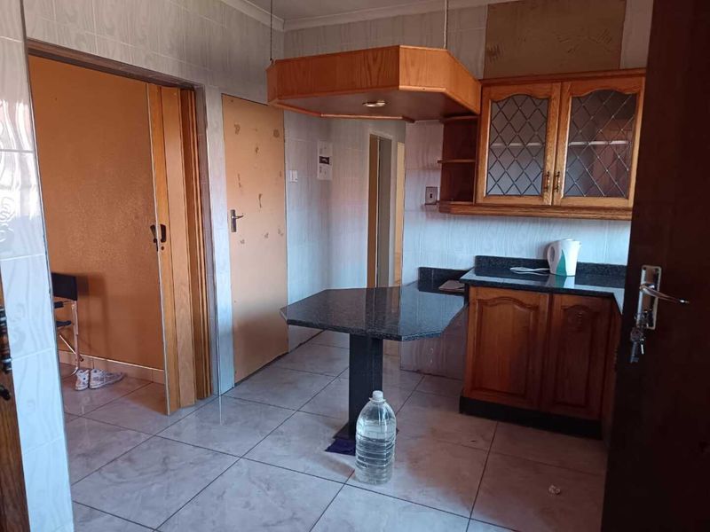 A dated kitchen featuring wooden cabinetry, granite countertops, a breakfast bar, and tiled flooring, offering potential for a modern renovation.
