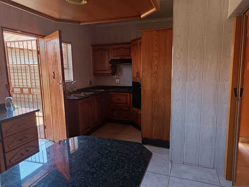 A functional kitchen featuring traditional wooden cabinetry, granite countertops, built-in oven, and tiled finishes, offering a classic layout with direct outdoor access.