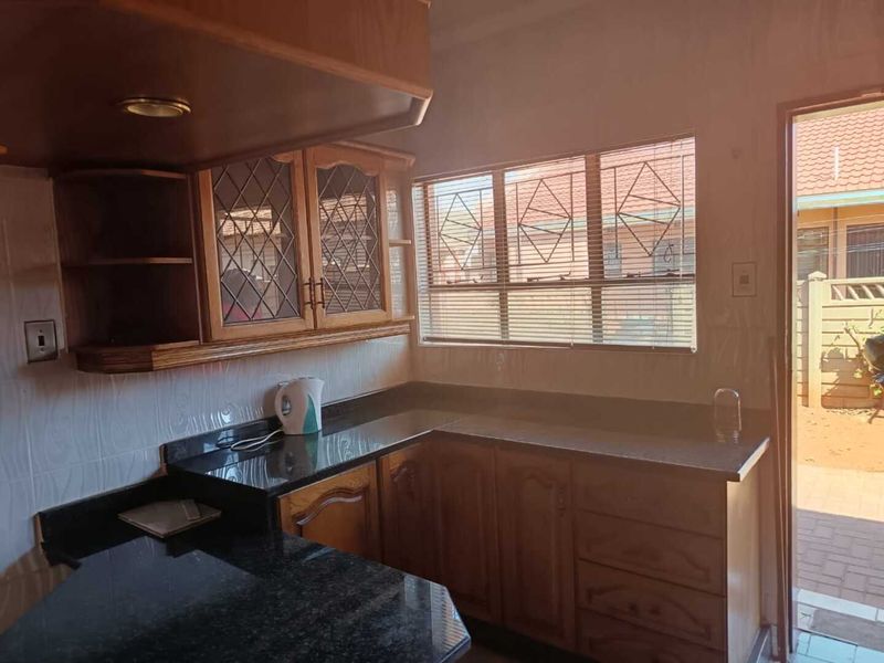 A functional kitchen featuring traditional wooden cabinetry, dark granite countertops, and tiled walls, with direct access to the exterior.