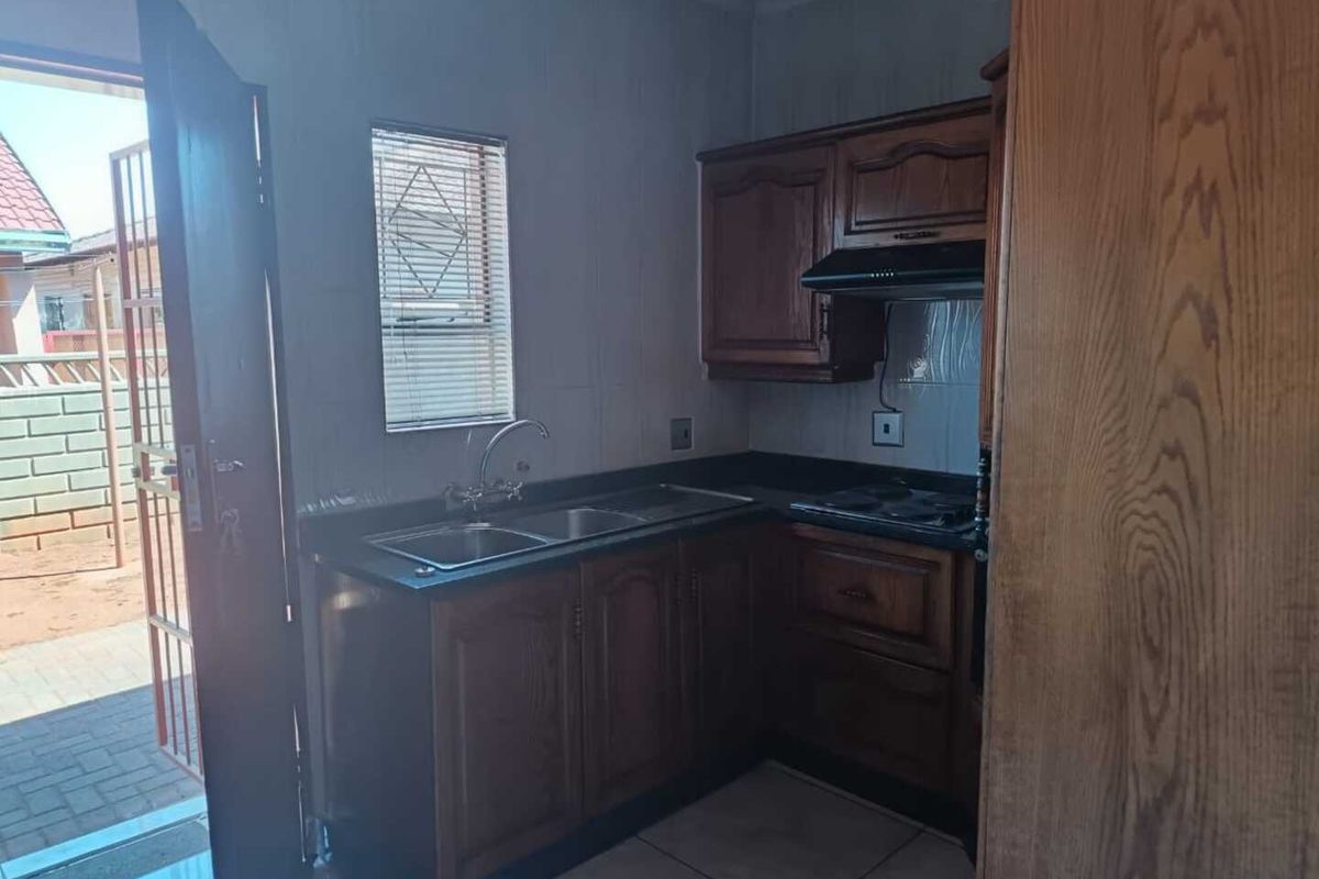 A functional kitchen featuring built-in wooden cabinetry, a double basin sink, and a fitted hob with an extractor fan, leading directly to an outdoor area.
