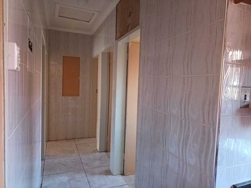 A tiled hallway featuring ceramic floor and wall tiles, showing signs of incomplete finishes and missing wall tiles requiring maintenance.