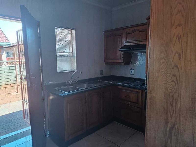 A functional kitchen featuring built-in wooden cabinetry, a double basin sink, and a fitted hob with an extractor fan, leading directly to an outdoor area.