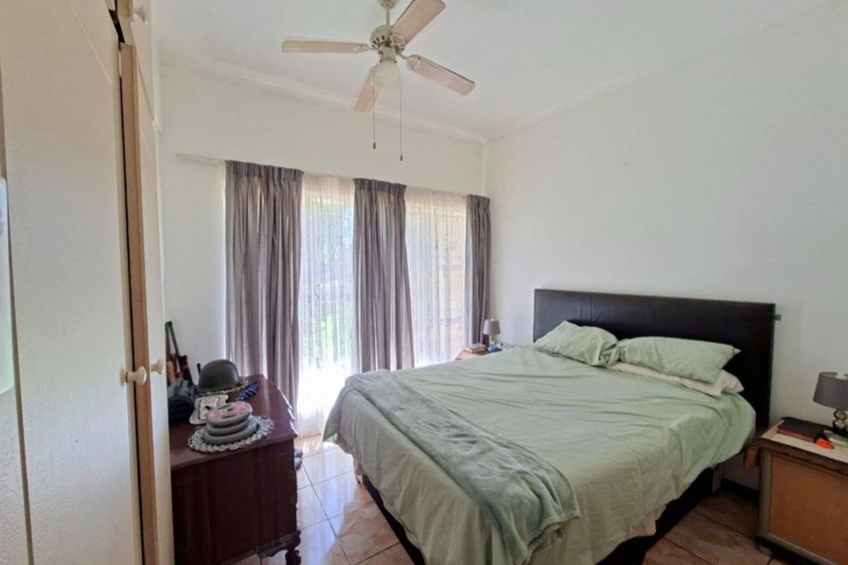 A functional bedroom featuring tiled flooring, a ceiling fan, and built-in storage cupboards with natural light from the window.
