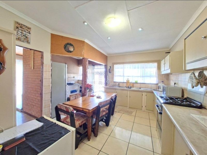 Open-plan kitchen and dining area featuring tiled flooring, built-in cabinetry, gas hob, and integrated oven, offering a functional layout with potential for modernization.