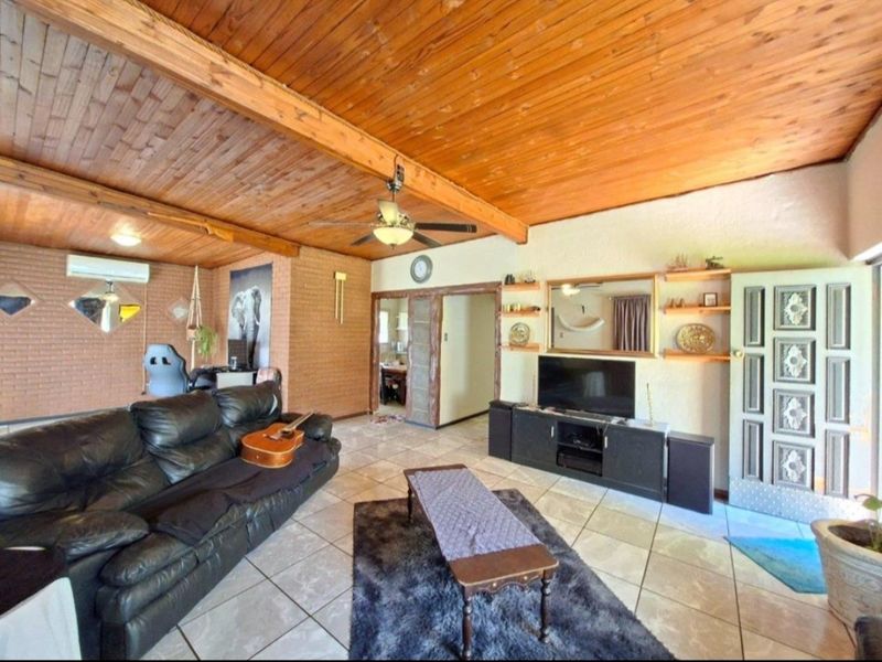 Spacious living room featuring a high exposed timber beam ceiling, tiled flooring, and an exposed brick feature wall with integrated air conditioning.