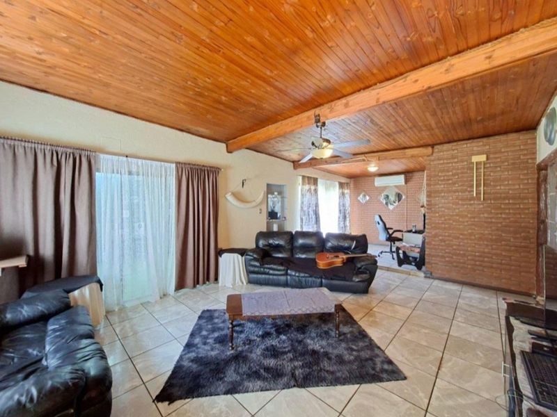 Spacious living area featuring exposed timber ceilings, brick feature wall, ceramic floor tiles, and direct access to the outdoors via sliding glass doors.
