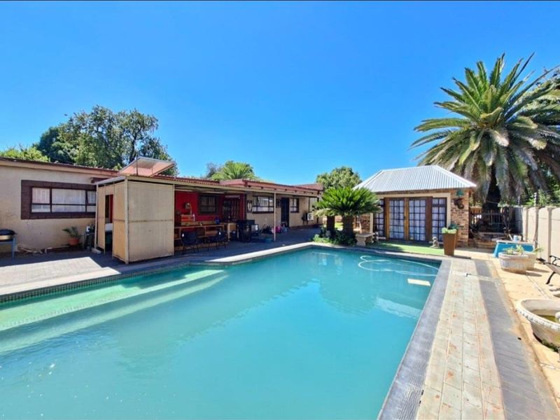 Outdoor pool area featuring a swimming pool, paved surround, and a covered patio area adjacent to the main dwelling and outbuilding.