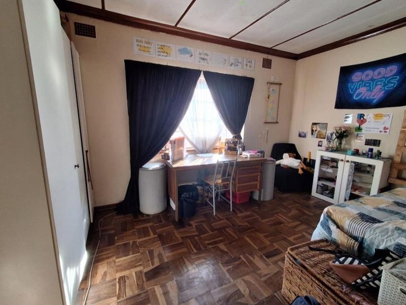 A bedroom featuring classic parquet flooring, a built-in cupboard, and a window with dark curtains.