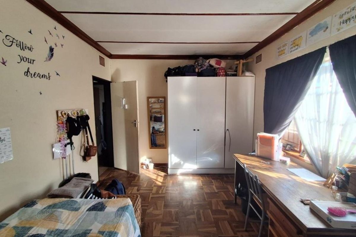 A bedroom featuring classic parquet flooring, a built-in wardrobe, and natural light through the window.