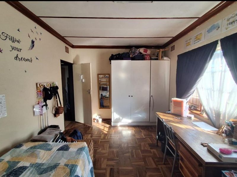 A bedroom featuring classic parquet flooring, a built-in wardrobe, and natural light through the window.
