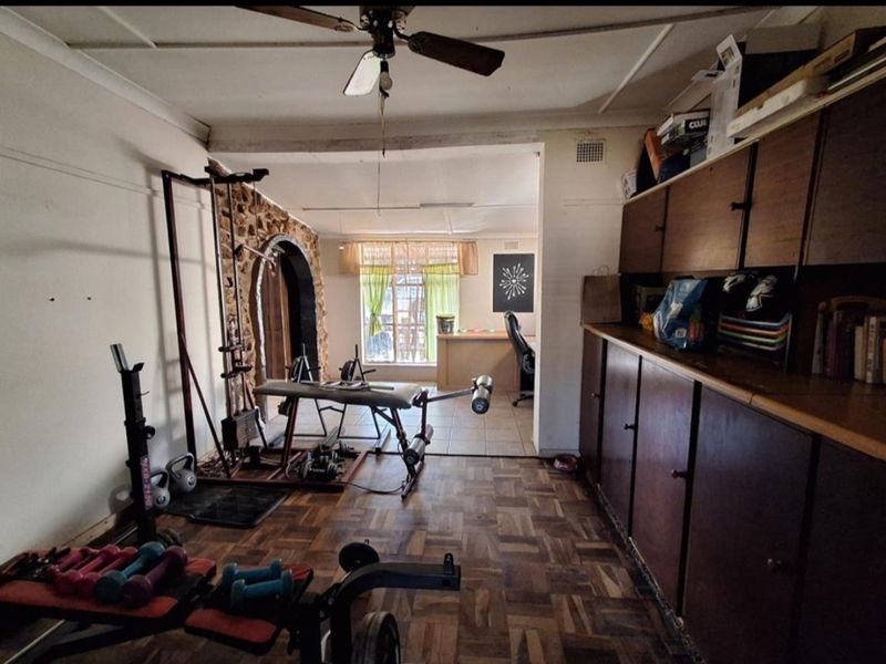 A multi-purpose room featuring parquet flooring, built-in storage cabinetry, and a stone feature wall, currently utilized as a home gym space.