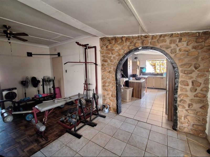 A multi-purpose room featuring a stone accent wall with an arched opening leading into the kitchen, finished with a mix of tile and parquet flooring.